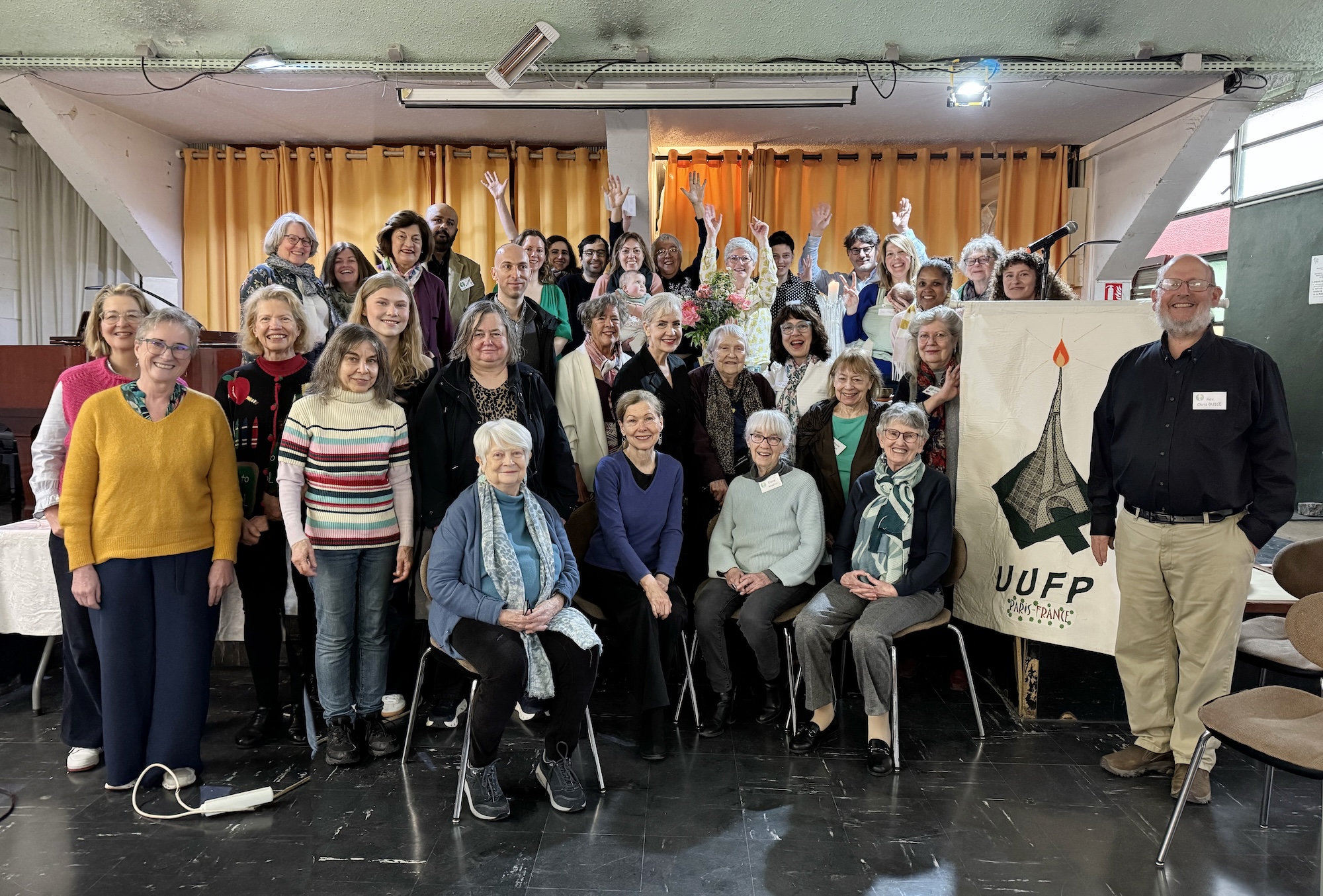 A group of Unitarian Universalists gathered for a photo indoors. Many are smiling. Some in the back row have their arms raised.